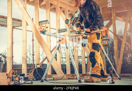 Appaltatore caucasico nel suo 40s taglio piccoli elementi di legno. Struttura di scheletro di legno della costruzione della casa. Foto Stock