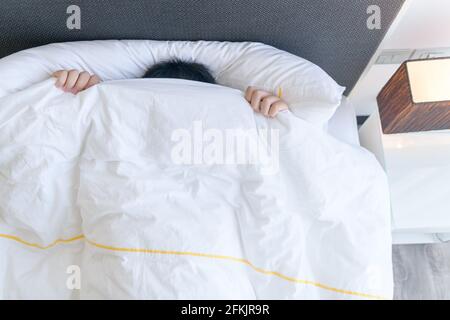 Ragazzo pigro che copre il viso con coperta mentre si trova a letto a casa, Lazy per svegliarsi concetto Foto Stock