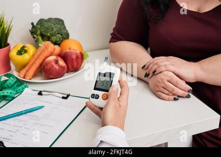 Misurazione della glicemia. Nutrizionista usando il glucometro testa lo zucchero di anima della donna in sovrappeso, controllo di prevenzione del diabete Foto Stock