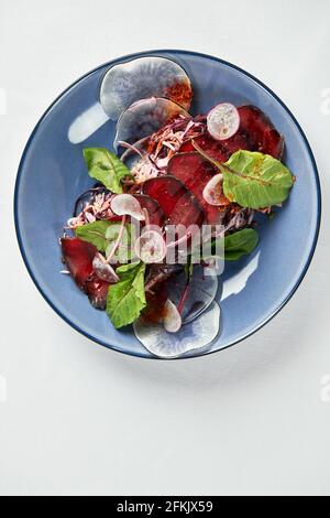 Insalata estiva di barbabietole con rucola, radicchio, formaggio morbido e noci su piatto condimento e spezie su piatto blu, spazio copia, vista dall'alto. Foto Stock
