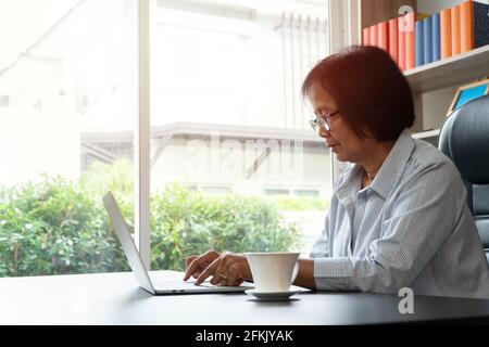 Happy Senior Asian utilizzando il computer portatile per il calcolo e prendere nota delle spese giornaliere. Concetto di stile di vita, apprendimento e finanza Foto Stock