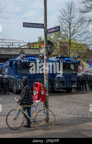 Amburgo, Germania - 1 maggio 2021: Cannoni ad acqua e polizia di rivolta al fianco di una manifestazione il giorno di maggio, Festa del lavoro. Persona con vintage bike crossing Foto Stock