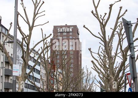 Colonia, NRW, Germania, 05 03 2021, vista sul vecchio edificio con IL marchio SATURN su di esso, alberi senza foglie in primo piano Foto Stock