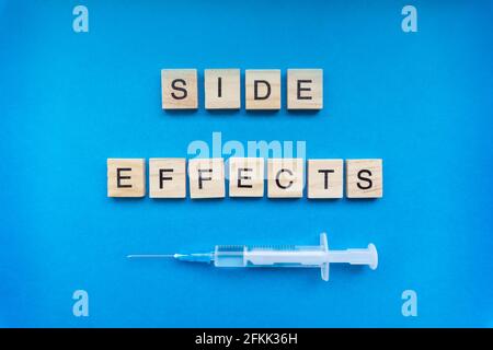 Segno degli effetti collaterali con lettere di legno e una siringa su sfondo blu. COVID-19 concetto di rischio di vaccinazione Foto Stock