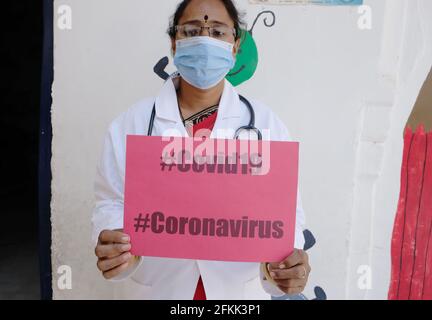 Una lavoratrice medica femminile indiana in una tenuta di maschera facciale Un poster con il testo COVID-19 CORONAVIRUS Foto Stock