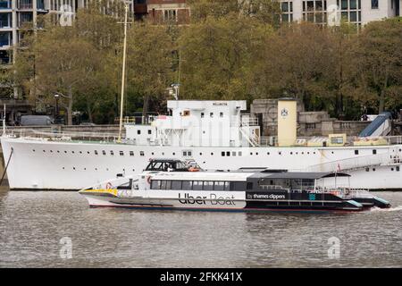 Uber Thames Boat Clipper passa per l'HQS Wellington sul Tamigi, Londra, Inghilterra, Regno Unito. Foto Stock