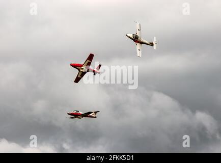 Getti rossi e bianchi che volano in formazione attraverso un grigio cielo con una tempesta estiva che sta per iniziare Foto Stock