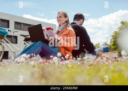 studente seduto in erba di fronte al palazzo universitario dando pollici in su Foto Stock