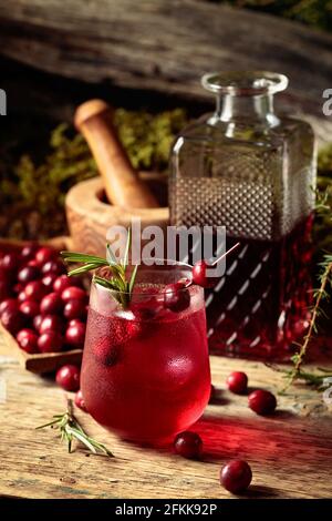 Cocktail gin tonic con mirtilli rossi, rosmarino, branca di ginepro e ghiaccio su un vecchio tavolo di legno. Foto Stock