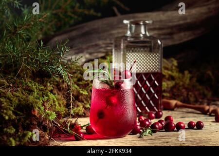 Cocktail gin tonic con mirtilli rossi, rosmarino, branca di ginepro e ghiaccio su un vecchio tavolo di legno. Foto Stock