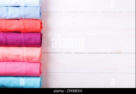 Primo piano di abiti colorati arrotolati con cura per risparmiare spazio sui bagagli, una pila di rotoli di t-shirt in cotone di diversi colori pastello su un tavolo di tessitura in legno. Foto Stock