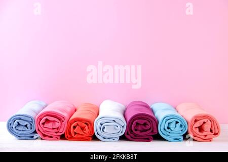 Primo piano di abiti colorati arrotolati con cura per risparmiare spazio sui bagagli, una pila di rotoli di t-shirt in cotone di diversi colori pastello su un tavolo di tessitura in legno. Foto Stock