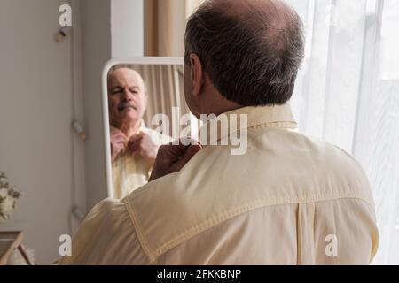 Uomo maturo che guarda nello specchio a casa Foto Stock
