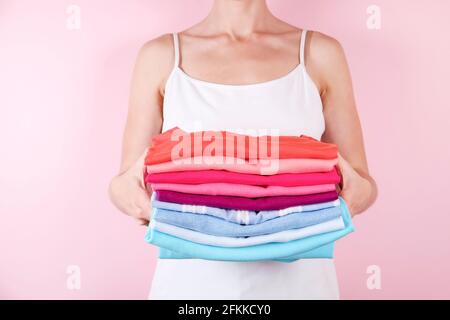 Primo piano di attraente giovane donna che regge pila di camicie perfettamente ripiegate multicolore. Femmina con mucchio di abiti di diverso colore nelle sue mani su pal Foto Stock