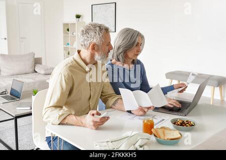 Coppia di età media che paga le fatture finanziarie in linea usando il calcolatore a casa. Foto Stock