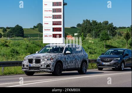 BMW X5 „Erlkönig", termine tedesco per un modello di preproduzione camuffato, passando per cartellone con i prezzi della benzina o della benzina vicino a Eurorastpark Jettingen Foto Stock