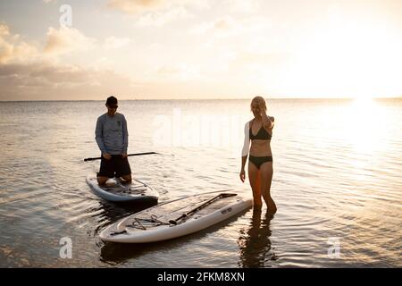 Due persone su una spiaggia alle Hawaii si stanno preparando a. paddleboard al tramonto Foto Stock