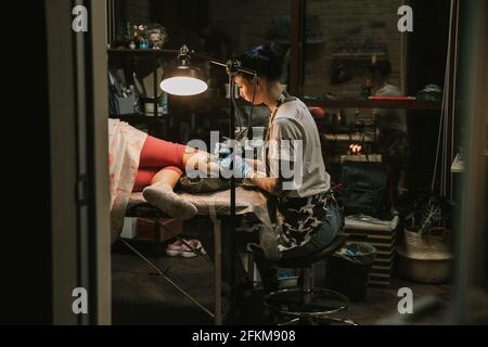 Ritratto di un maestro di tatuaggio donna che mostra un processo di creazione tatuaggio su una mano sotto la luce della lampada. Foto Stock