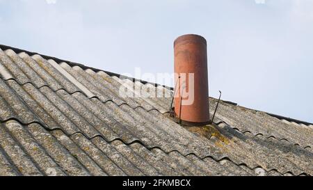 Camino sotto forma di tubo sul vecchio tetto di ardesia del fienile, parzialmente coperto di lichene giallo, contro il cielo Foto Stock