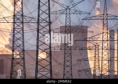 Vista attraverso i tralicci elettrici sulla centrale alimentata a lignite con torri di raffreddamento a vapore al tramonto, Niederaussem, Nord Reno-Westfalia, Germania Foto Stock