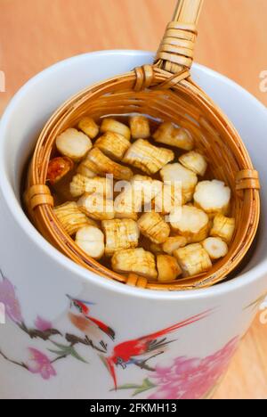 Ginseng-tè (Panax ginseng) in tazza, setaccio di bambù, radici tagliate, seng, panacea Foto Stock