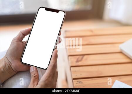 Vista dall'alto primo piano con le mani femminili che tengono lo smartphone con schermo bianco vuoto. Donne mani spazio di lavoro, primo piano mano tenendo lo smartphone schermo vuoto per t Foto Stock