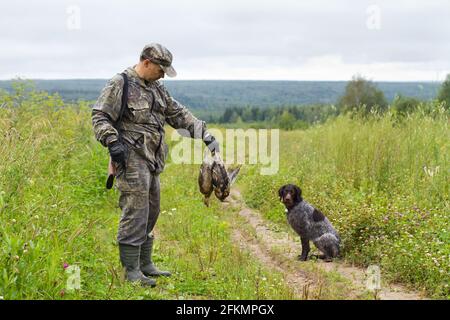 hunter con il suo gundog è sulla strada con preda in mano Foto Stock