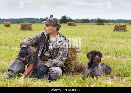 hunter con il suo gundog che riposa sull'hayfield durante il caccia d'autunno Foto Stock