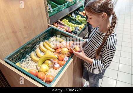 Una bambina sceglie le mele e le banane confezionate singolarmente nel negozio. Foto Stock