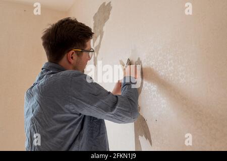 Uomo strappando la vecchia carta da parati dalla parete che si prepara per la casa ridecorazione Foto Stock