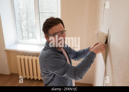 Uomo strappando la vecchia carta da parati dalla parete che si prepara per la casa ridecorazione Foto Stock