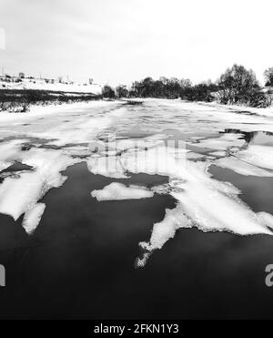 Bianco e nero panoramico paesaggio rurale invernale o primavera con galleggianti su pezzi di superficie dell'acqua di ghiaccio fondente Foto Stock