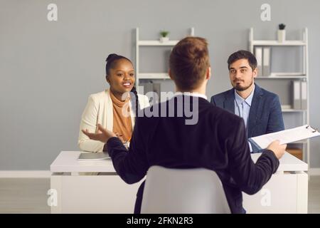 Una giovane coppia sposata ascolta attentamente un consulente finanziario della banca durante una riunione in ufficio. Foto Stock