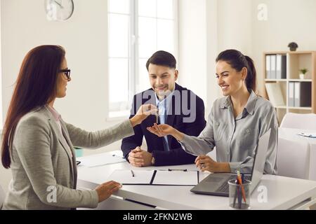 Agente immobiliare dà le chiavi alla sua nuova casa ad una coppia sposata ad una riunione nell'ufficio. Foto Stock
