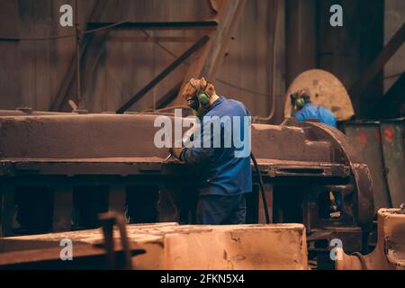 Il lavoratore in officina lavora una grande parte di ghisa dopo la fusione in un impianto di fonderia metallurgica. Foto Stock