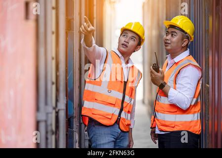 Due operai o ingegneri che cercano e puntano qualcosa dentro magazzino dei contenitori Foto Stock