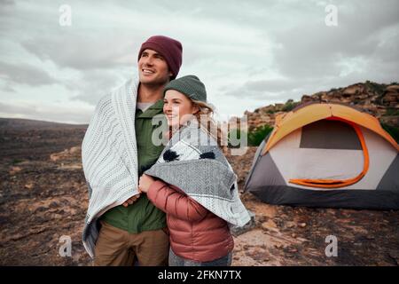 Uomo e donna romantici avvolti in una coperta in piedi insieme tenda esterna in montagna che guarda alla bella natura Foto Stock