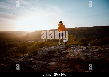 Vista posteriore di un giovane atleta di forma fisica maschile che attraversa la roccia sentiero di montagna Foto Stock