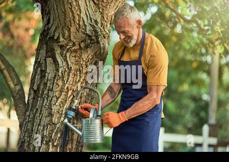 Felice uomo caucasico medio invecchiato che riempie annaffiatoio può Foto Stock