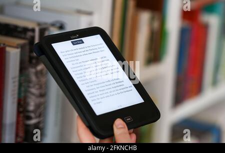 Berlino, Germania. 18 Apr 2021. ILLUSTRAZIONE - UNA donna tiene un lettore di eBook nelle sue mani. Sullo sfondo, i libri stampati su una libreria. Credit: Jens Kalaene/dpa-Zentralbild/ZB/dpa/Alamy Live News Foto Stock