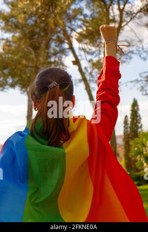 Una ragazza transgender con la bandiera gay con il suo pugno sollevato. Persone autentiche non binarie. Giornata dell'orgoglio gay Foto Stock