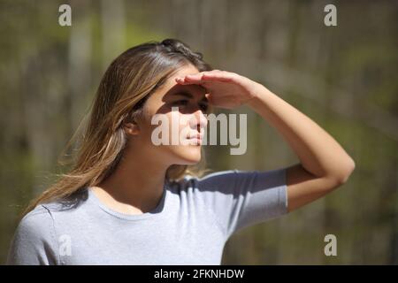 Donna che protegge dal sole con la mano che guarda via dentro una foresta Foto Stock