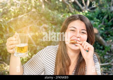 bella e bella ragazza ride mentre si mangia una fetta di pizza seduta al tavolo del ristorante all'esterno Foto Stock