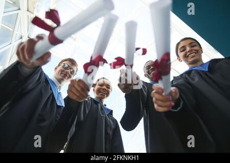 Vista a basso angolo del gruppo di laureati in possesso di diplomi alla fotocamera mentre si è in piedi all'interno Foto Stock