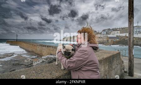 Donna che tiene il cane soffiato dal vento a Porthleven, Cornovaglia Foto Stock