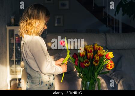 Carino bella bambina che fa bouquet di fiori. Bambina che mette tulipano al bouquet in un vaso. Fare un mazzo di regali per la festa della mamma Foto Stock