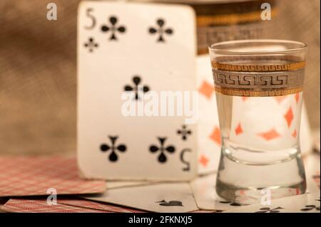 Carte da gioco e un bicchiere di vodka su un tavolo coperto di burlap grossolano. Primo piano, messa a fuoco selettiva. Foto Stock