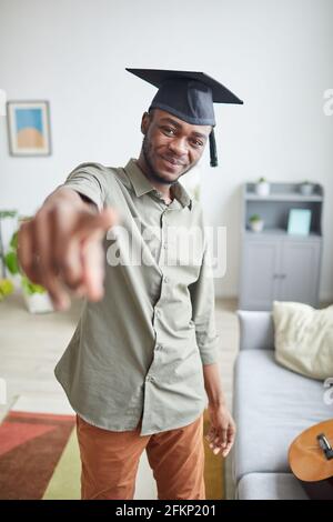 Ritratto verticale di un giovane afro-americano che indossa una cuffia graduata e. puntare verso la telecamera nell'abitacolo Foto Stock