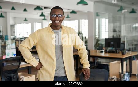 Sorridente giovane uomo d'affari africano in piedi dalla sua scrivania in un ufficio Foto Stock