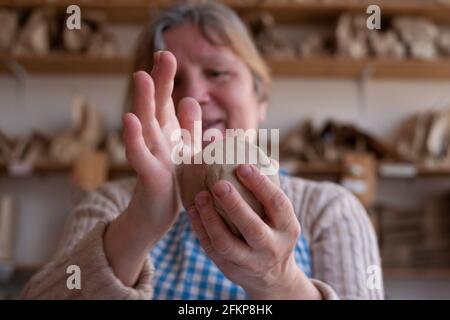 Mani femminili che tengono una sfera fatta di argilla per iniziare a lavorare sulla ruota Foto Stock